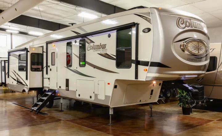 A large, cream and gray Columbus fifth-wheel RV is shown indoors, with slides extended and steps deployed. Ideal for rv rental.. Palomino Columbus 2019