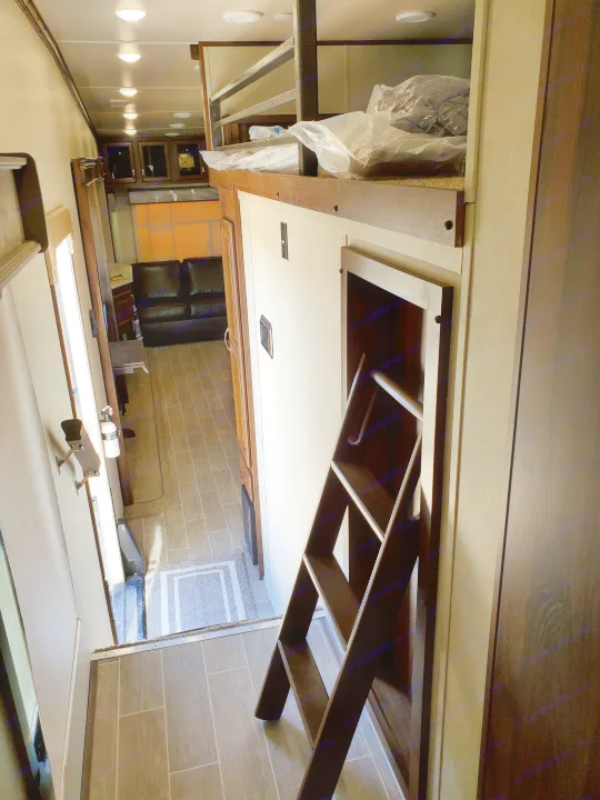 Inside an RV rental: View of a hallway with a ladder leading to a loft bed, extending to a living area with a dark sofa.. Palomino Columbus 2019