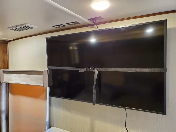 RV rental interior features a large TV, secured by a strap for travel, with an overhead light, power outlet, and ceiling vent.. Palomino Columbus 2019