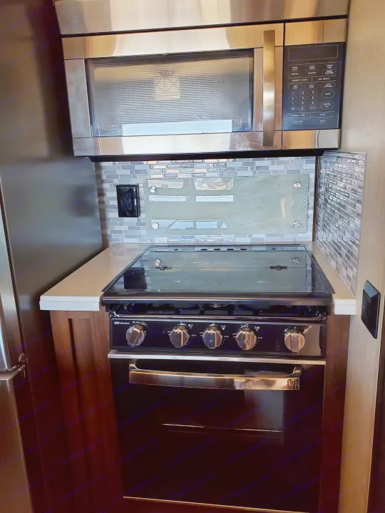 Modern RV rental kitchen setup with a stainless steel microwave, tiled backsplash, and built-in Suburban oven/cooktop.. Palomino Columbus 2019