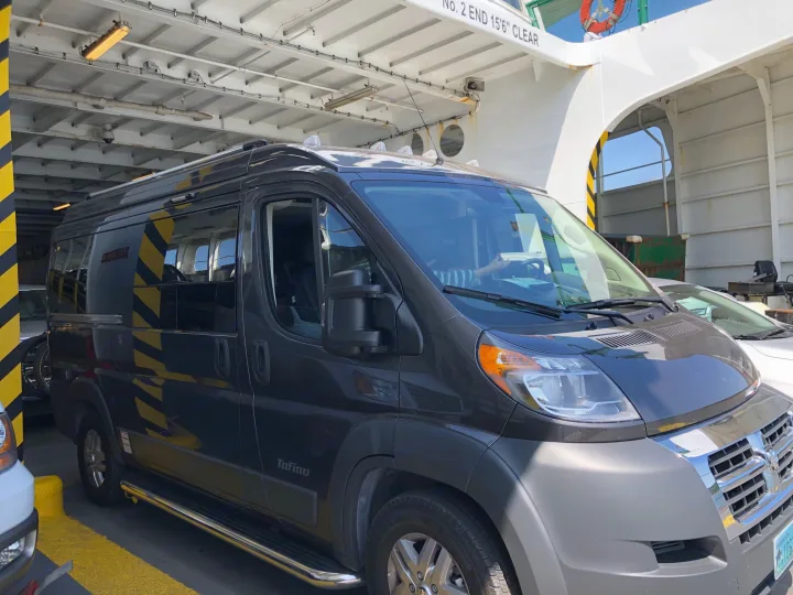 A dark gray Tofino rv rental van from Washington State is parked inside a vehicle ferry, ready for an adventure.. PleasureWay Tofino 2019