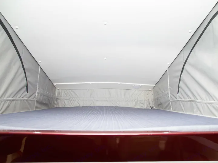 Inside a spacious RV rental pop-top camper: an elevated bed with a striped mattress, overhead lighting, and side speaker.. PleasureWay Tofino 2019