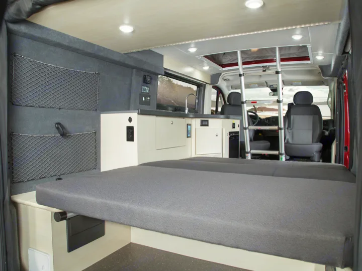 RV rental interior: comfy bed, kitchenette, storage, and a ladder to a pop-top, with a scenic front view.. PleasureWay Tofino 2019