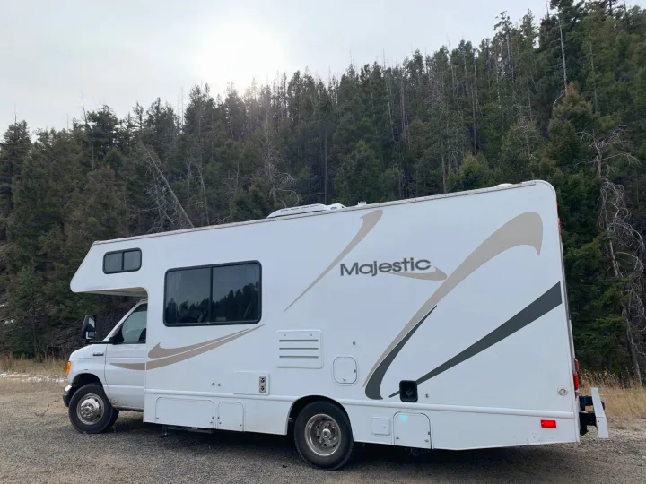 White Majestic RV rental motorhome on a gravel road, surrounded by evergreen trees in the wilderness.. Majestic Leisure Craft Tourer Ii 2007
