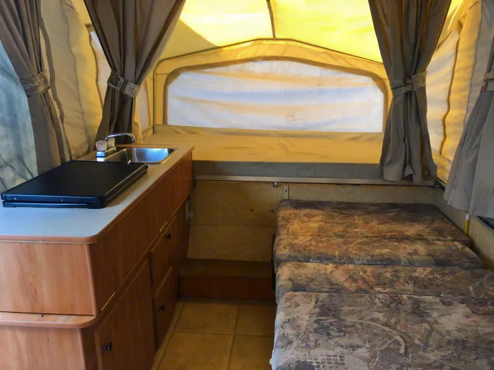 Interior of an **RV rental** pop-up camper, featuring a kitchenette with sink, and two distinct sleeping berths.. Starcraft St 2006