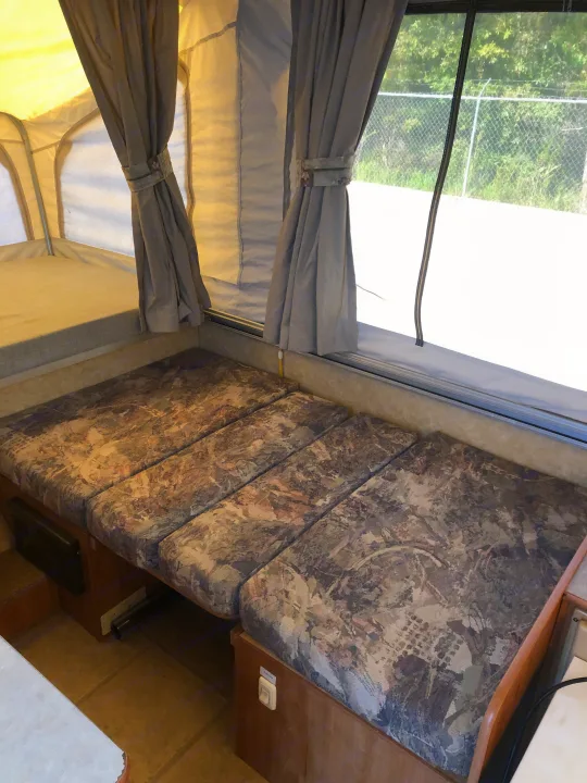 Interior of an RV rental pop-up camper showing a bed/seating area with patterned cushions and tied-back curtains.. Starcraft St 2006