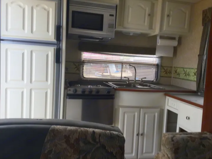 Inside an RV rental: a compact kitchen with a fridge, microwave, stove, and sink, perfect for road trips.. Max Lite ML26RK 2006