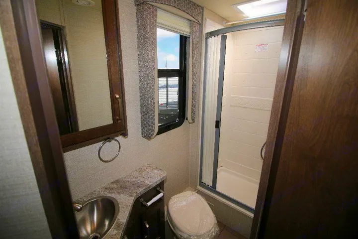 RV rental bathroom: Compact shower, sink, and toilet with mirrored cabinet, window, and patterned valance.. Jayco Melbourne 2019