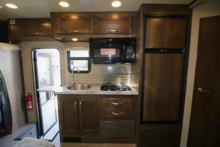 RV rental interior: A compact kitchen with sink, stovetop, microwave, refrigerator, and wood cabinets.. Jayco Melbourne 2019