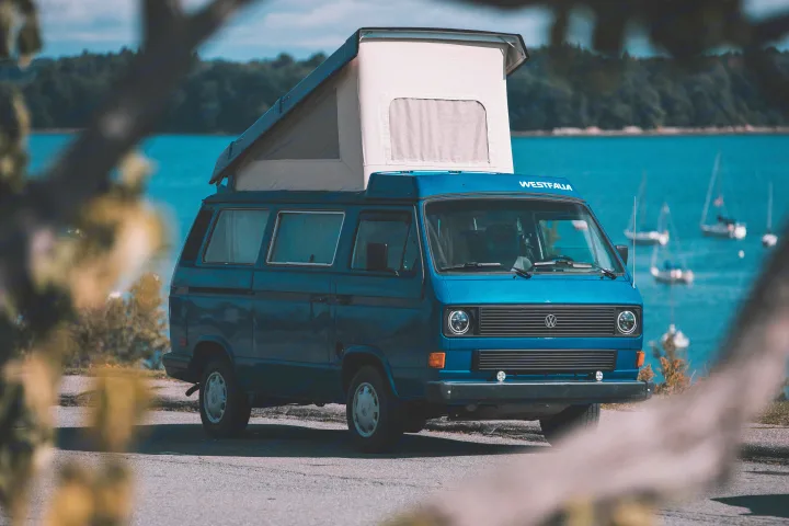Blue VW Westfalia pop-top camper van for your next RV rental adventure, parked by a scenic lake with sailboats.. Volkswagen T3 Westfalia 1984