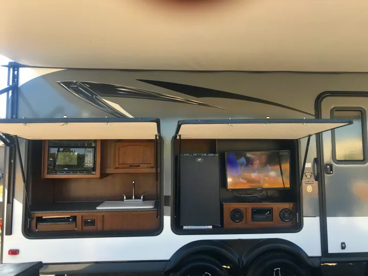 This rv rental showcases its outdoor kitchen with microwave & sink, and an entertainment center with TV & fridge for outdoor fun.. Jayco Jay Feather 2016