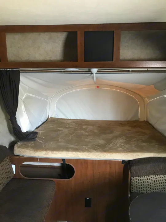 Cozy RV rental interior: a plush bed in the pop-up tent area, flanked by dinette seating, ready for travel.. Jayco Jay Feather 2016