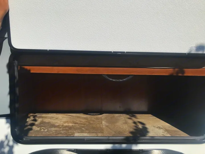 Open exterior storage compartment on an RV rental, revealing an empty, wood-lined interior and textured door.. Jayco Jay Feather 2016