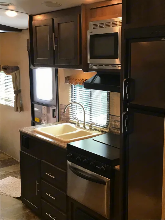 RV rental kitchen interior: sink, microwave, stove, fridge, and cabinets in a compact, well-equipped space.. Forest River Surveyor 2015