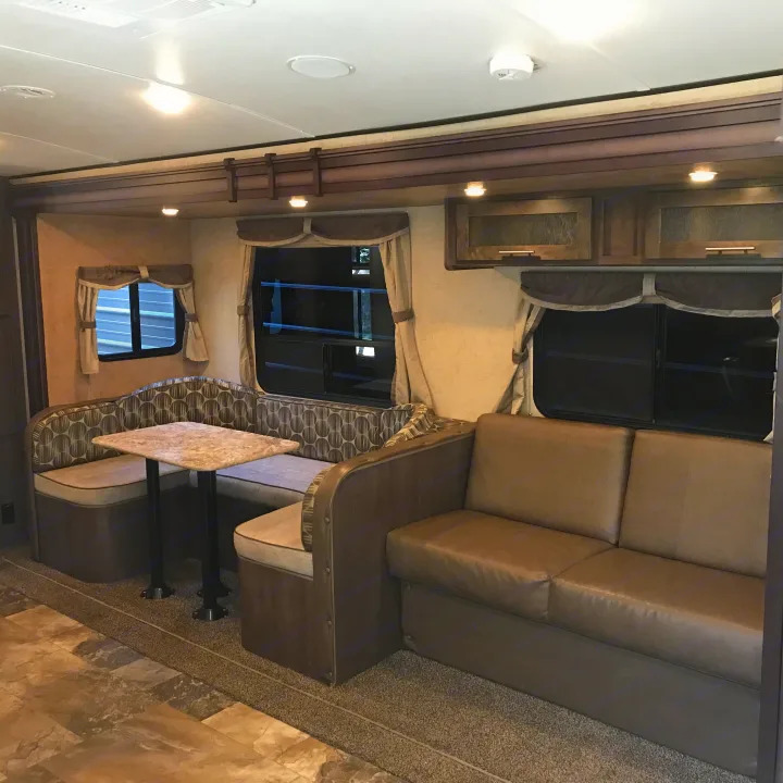 An RV rental living area with a dinette booth, sofa, decorative curtains, overhead cabinets, and ample lighting.. Forest River Surveyor 2015