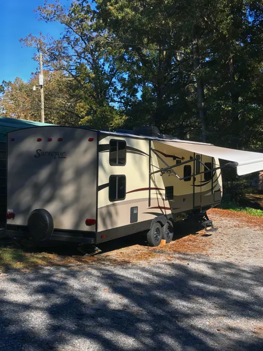 Beautiful Surveyor travel trailer, perfect for an RV rental adventure, with its awning extended on a sunny gravel lot.. Forest River Surveyor 2015