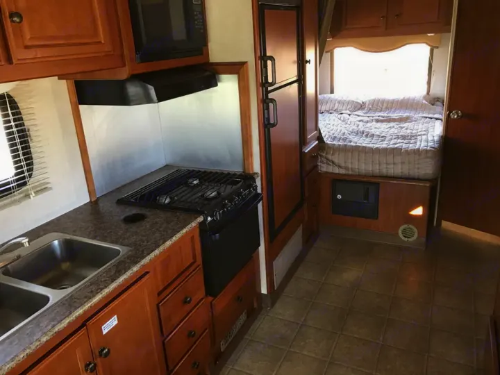 RV rental interior: functional kitchen with stove & sink, leading to a cozy bed area. Ideal for adventures.. Fleetwood Tioga Ranger 25G 2011