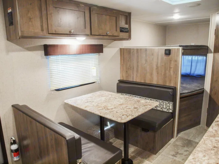 RV rental interior showcasing a dinette with wood-look table, benches, overhead cabinets, and partially hidden bunk beds.. Dutchmen Aspen Trail LE 1950BH 2020
