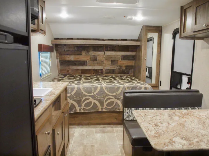 Spacious RV rental interior featuring a cozy bed, compact kitchen, and dinette seating. Ideal for comfortable travel adventures.. Dutchmen Aspen Trail LE 1950BH 2020