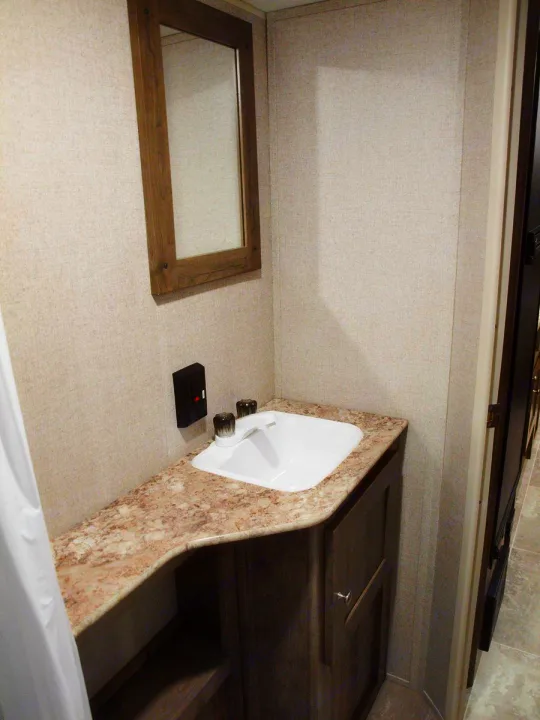 Inside an RV rental bathroom: compact vanity with sink, mirror, and wood cabinet storage.. Dutchmen Aspen Trail LE 1950BH 2020