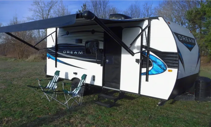White Dream travel trailer RV rental with an extended awning, two camping chairs on grass, ready for adventure.. Riverside Rv Dream 175BH 2018