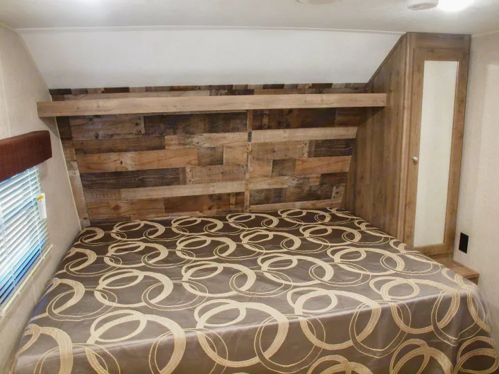 Cozy RV rental bedroom with a large bed, rustic wood headboard, window with blinds, and mirrored wardrobe, perfect for travel.. Dutchmen Aspen Trail LE 1950BH 2020
