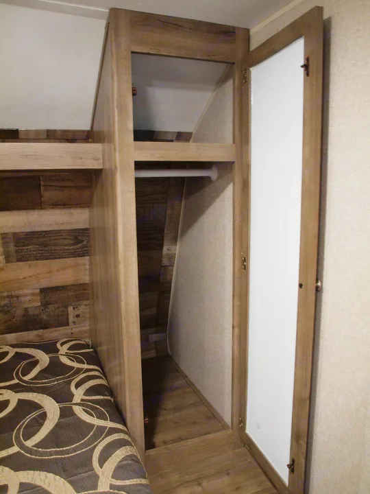 RV rental interior: a wood-grain cabinet structure with hanging rod & open door, next to a compact bed.. Dutchmen Aspen Trail LE 1950BH 2020