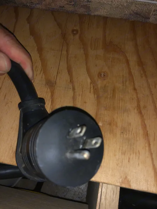 A hand holds a standard 3-prong electrical plug on wood, key for an RV rental's auxiliary power needs.. Starcraft St 2006