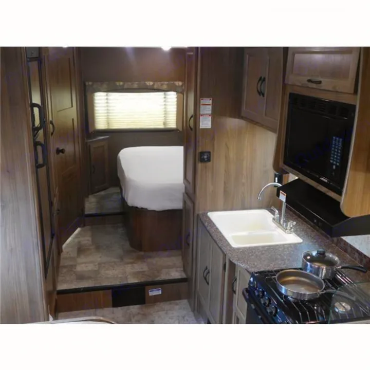 Inside an RV rental: a well-equipped kitchen with a stove, sink, and microwave, plus a comfortable bedroom area.. Coachmen Freelander 2017