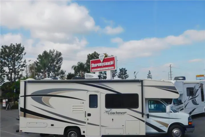 A white Coachmen Freelander RV, seen at an RV rental lot, with a 'Sharemycoach!' sign in the background.. Coachmen Freelander 2017