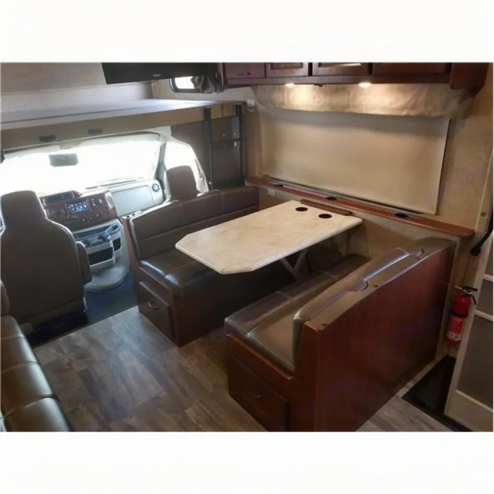 Inside an **RV rental**, showing a well-lit dining area with a table and benches, and the driver's cockpit beyond.. Forest-River Forester 2017