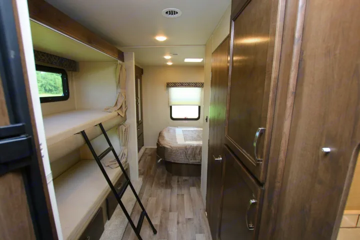 Spacious RV rental interior featuring cozy bunk beds, a clear path to the main bedroom, and ample storage for travel comfort.. Jayco Redhawk 2019