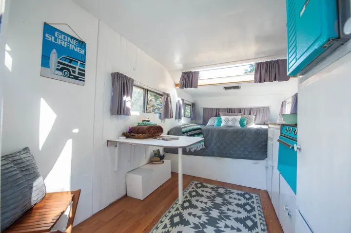 Experience a compact RV rental: featuring a bedroom, mini-kitchen, dining table, and surf-themed decor.. Custom Camper Trailer 1973