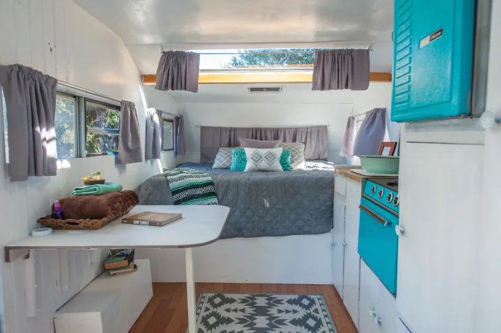 This inviting rv rental shows a cozy bed, neat kitchen with a teal stove, and a small dining area inside.. Custom Camper Trailer 1973