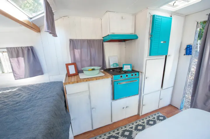 Cozy RV rental interior featuring a retro turquoise kitchen, comfortable bed, and white cabinets, ideal for travel.. Custom Camper Trailer 1973