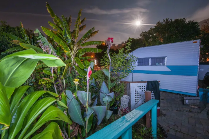 Moonlit tropical garden scene with a classic white and blue RV rental parked nearby, offering a unique outdoor stay.. Custom Camper Trailer 1973