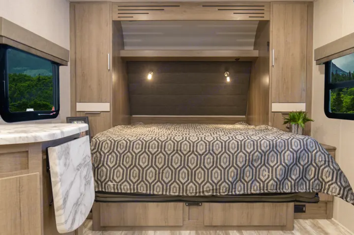 RV rental bedroom features a large bed, built-in storage, and reading lights. Scenic forest views from windows.. Grand Design Imagine XLS 19BWE 2020