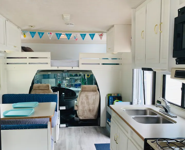 Inside an RV rental: a bright interior featuring a compact kitchen, dinette with blue seating, and comfy bunk beds.. Itasca Spirit 1999