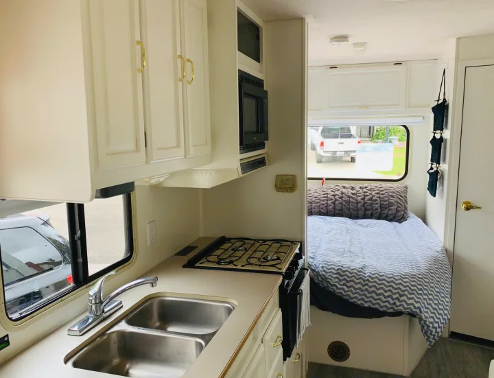 Cozy RV rental interior with a fully equipped kitchen (sink, stove, microwave) and a comfortable bed area.. Itasca Spirit 1999