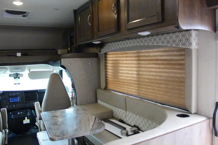 This RV rental interior features a modern dinette with integrated kitchen elements, an overhead bunk, and the front cab area.. Coachmen Freelander 2020