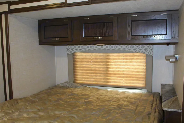 Cozy RV rental bedroom featuring a large bed, overhead storage, and a window with a pleated shade for comfortable travel.. Coachmen Freelander 2020