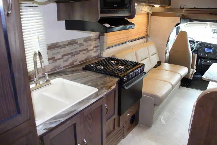 This RV rental interior showcases a functional kitchen with a double sink, stovetop, and microwave, alongside versatile dinette seating.. Coachmen Freelander 2020