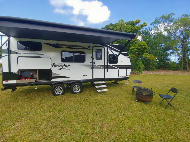 Imagine XLS RV rental camp setup: extended awning, outdoor kitchen, fire pit, chairs on lush green lawn.. Grand Design Imagine XLS 21BHE 2020