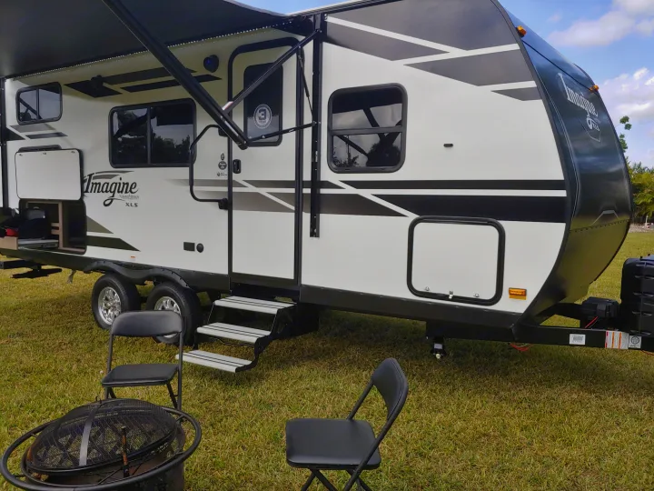Enjoy outdoor living with this Imagine XLS RV rental, featuring an extended awning, steps, fire pit, and chairs on lush grass.. Grand Design Imagine XLS 21BHE 2020