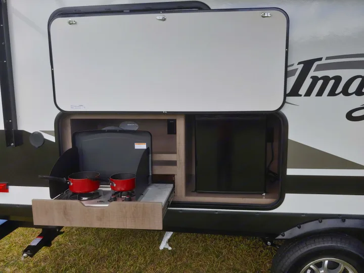 An RV rental featuring an open outdoor kitchen with a pull-out stove, two pots, and a compact refrigerator.. Grand Design Imagine XLS 21BHE 2020