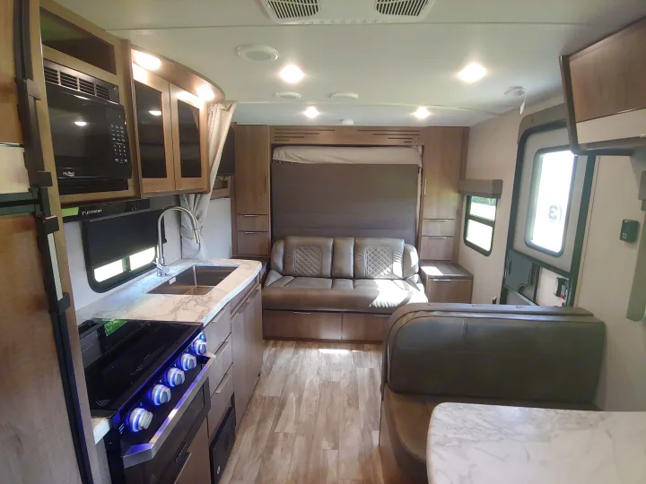 RV rental interior shows a modern kitchen, convertible sofa bed, and dining area with wood-look flooring.. Grand Design Imagine XLS 21BHE 2020