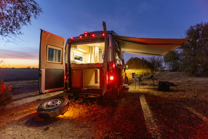 An illuminated RV rental with open back doors, showcasing its cozy interior and an outdoor camping setup at dusk. Ideal for adventure.. Hymer Other 2019