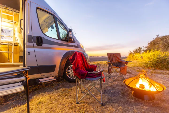 Enjoy a serene sunset campfire with an RV rental, cozy chairs, and a fire pit in a field. Perfect for outdoor adventure!. Hymer Other 2019