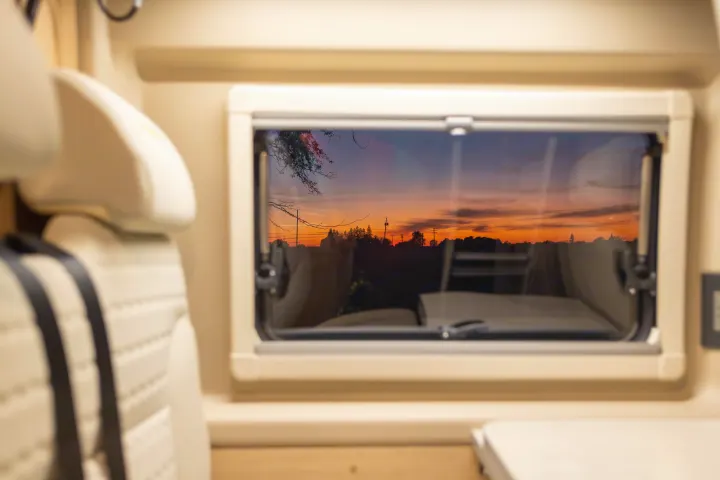 Inside a comfy RV rental, watch a vibrant sunset through the window, revealing trees, power poles, and warm sky hues.. Hymer Other 2019