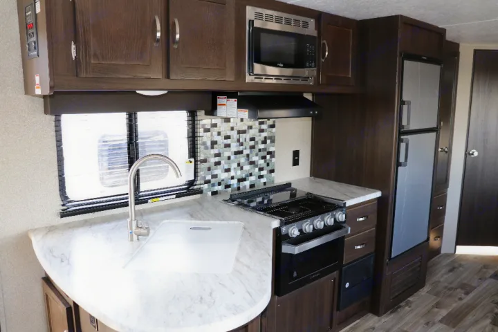 RV rental kitchen: This compact interior features a sink, stove, microwave, fridge, and ample cabinets.. Keystone Springdale 2020